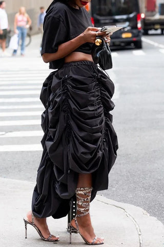 Person wearing a black outfit with a ruffled skirt on a city street.