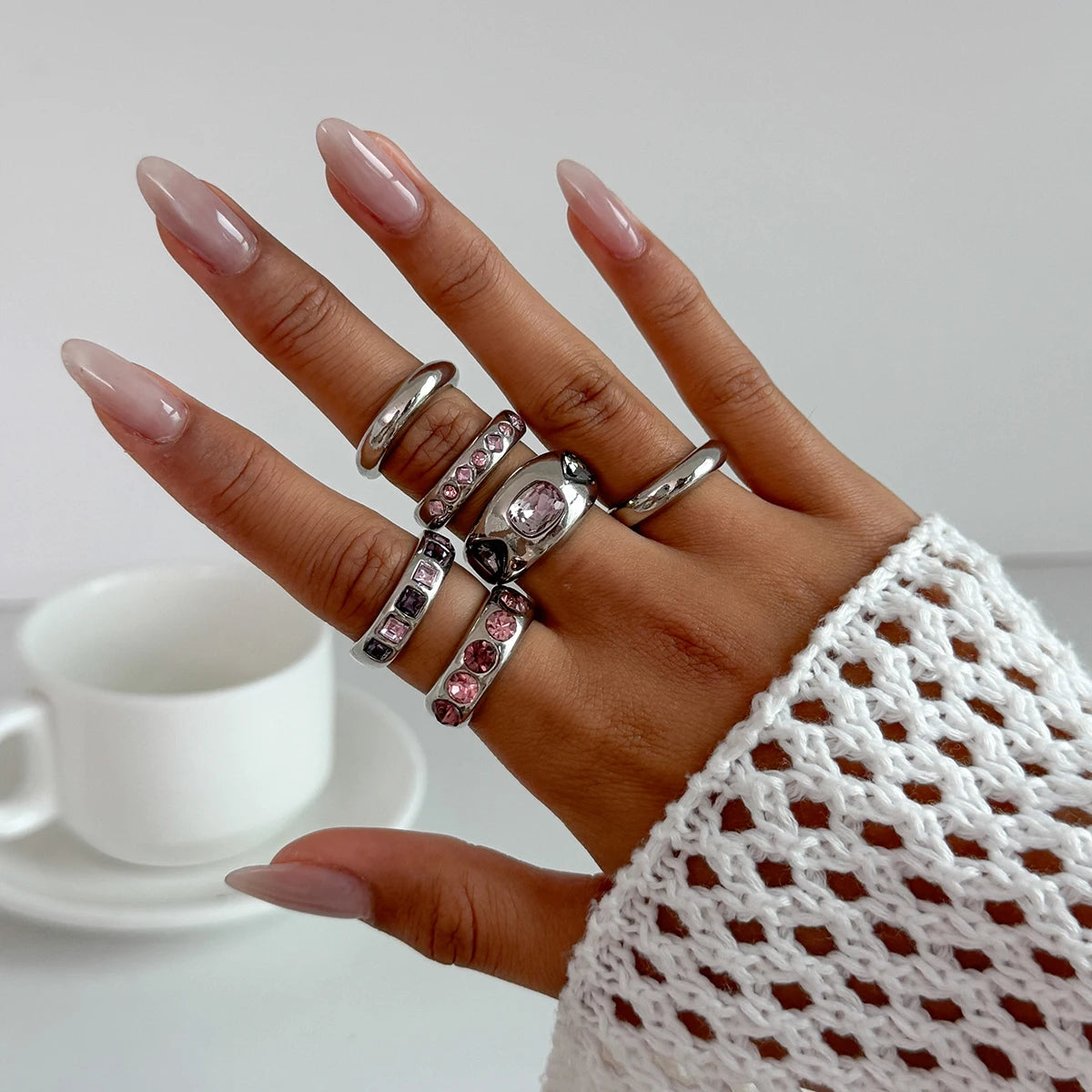 Hand wearing multiple rings with a blurred background of a white cup and saucer.